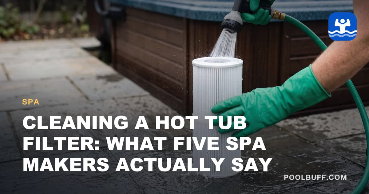 Hands in green rubber gloves rinsing a white pleated hot tub filter cartridge with a hose nozzle, the cartridge standing on wet stone pavers beside a hot tub cabinet
